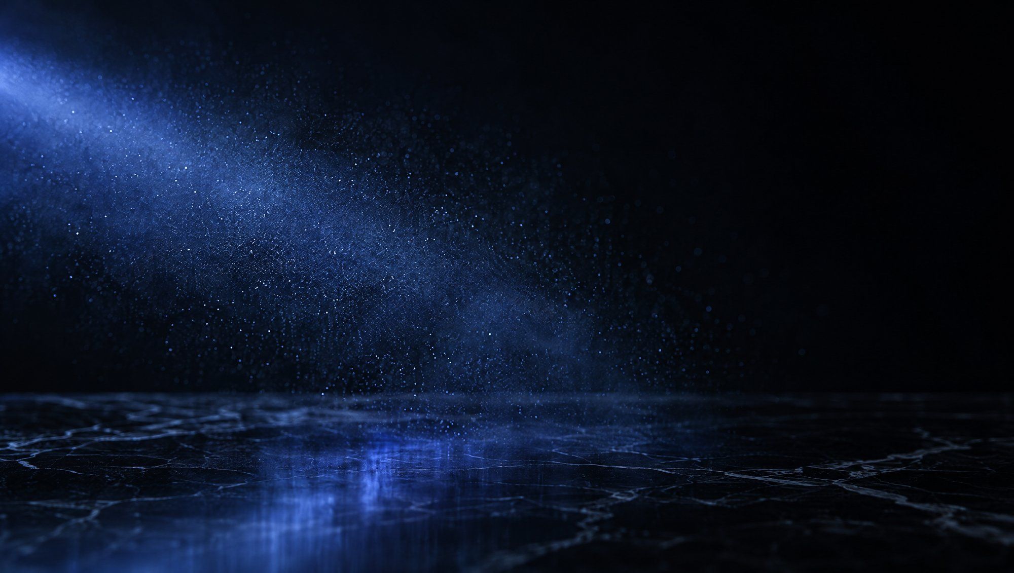 A fine mist of tiny droplets suspended in darkness above a dark marble surface, lit by a diagonal band of indigo light that reflects on the stone.