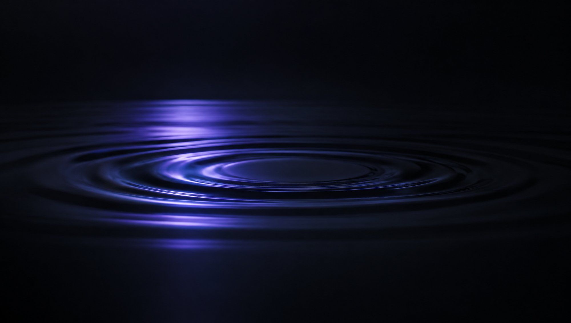 A still, dark water surface with one circular ripple spreading across it, reflecting a soft band of indigo light.
